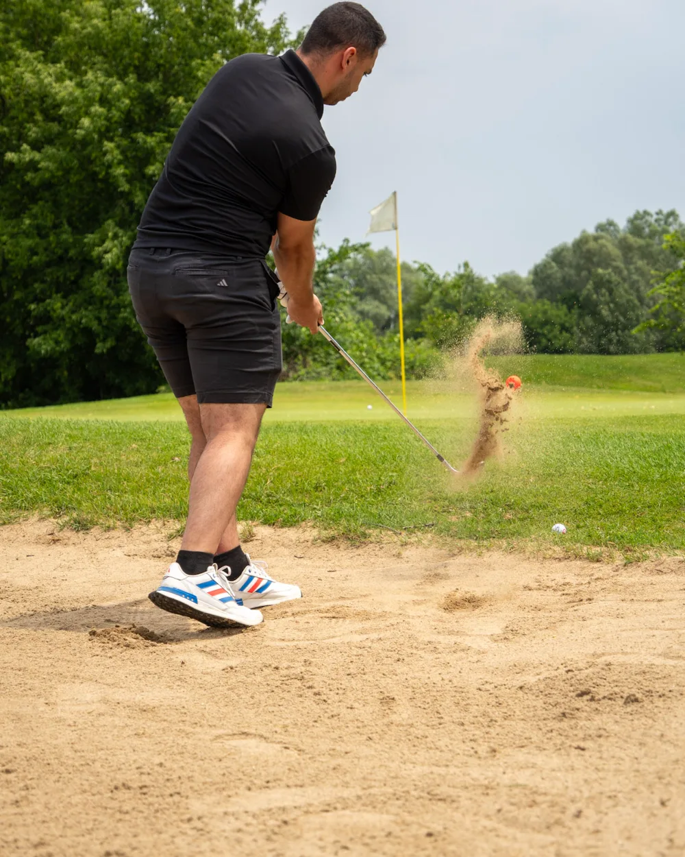 A golfer playing out of a greenside bunker, sand in the air.